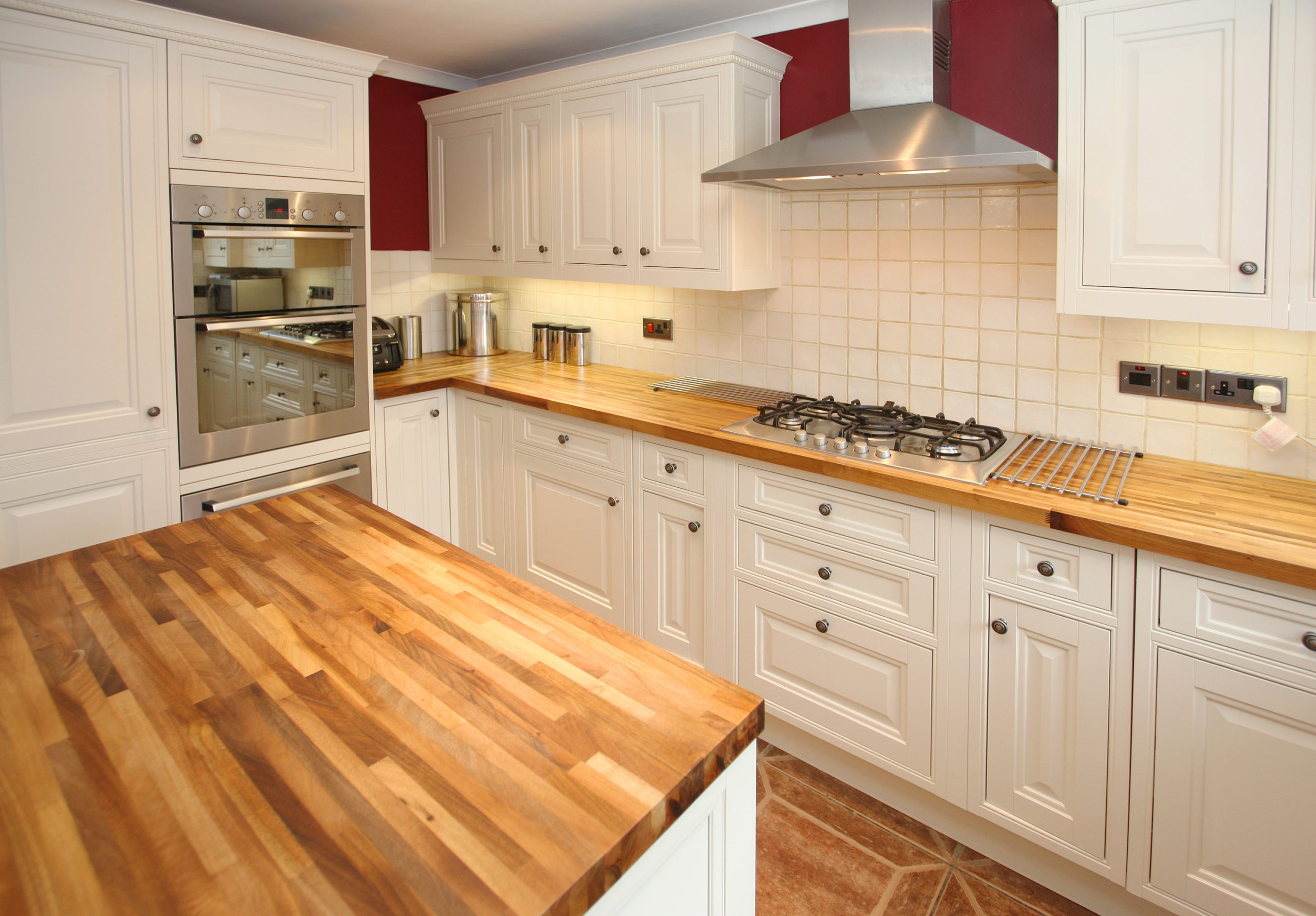 Bright traditional kitchen after Worktop Refinishing in Gants Hill, featuring smooth oak butcher-block worktops and a warm terracotta ceramic tiled floor.