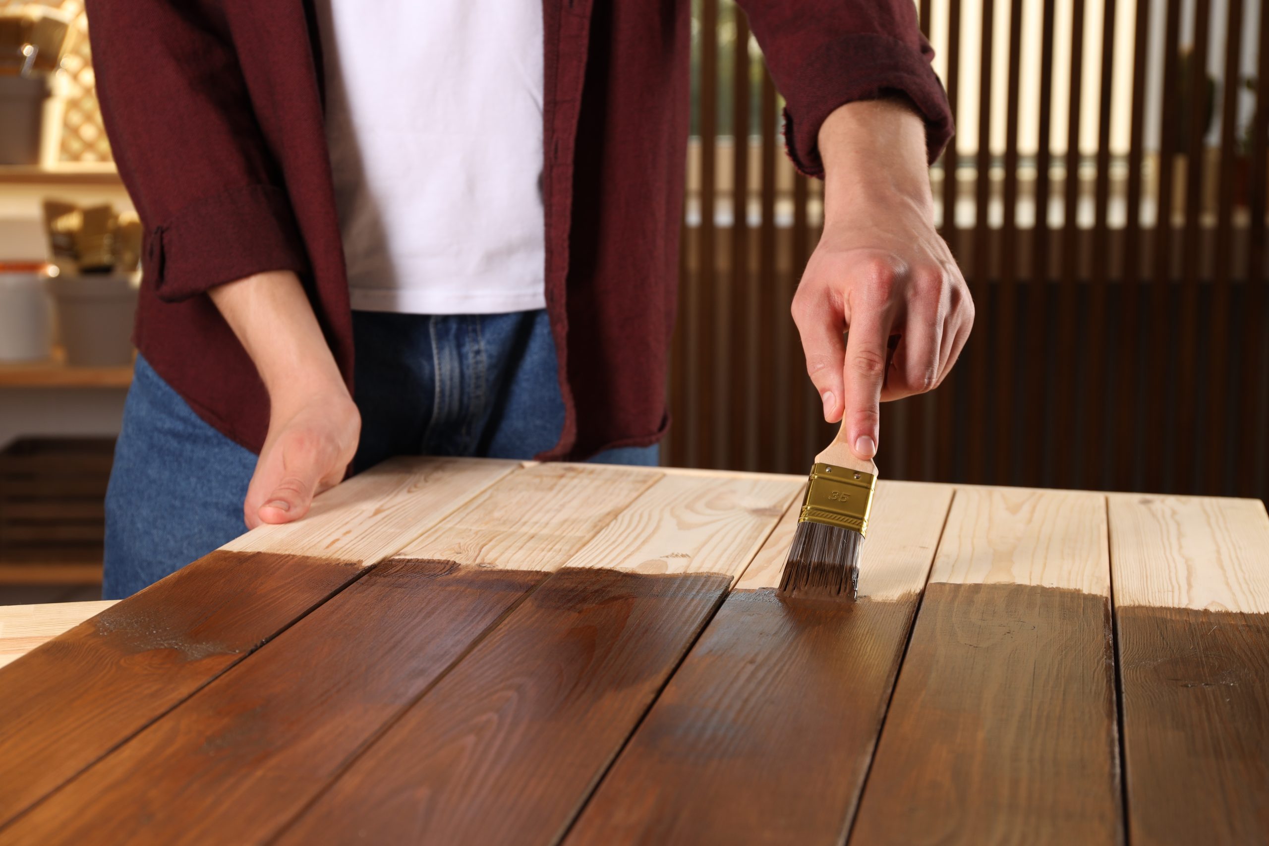 Worktop Refinishing in Gants Hill on a solid pine wood worktop, with a person brushing dark stain across pine plank boards matching a pine plank floor finish.